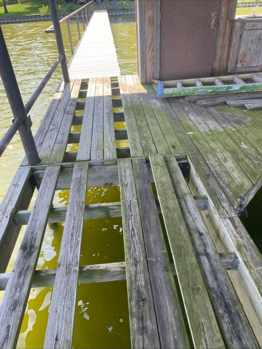 Damaged dock deck with missing boards, deteriorated wood and exposed framing over the water