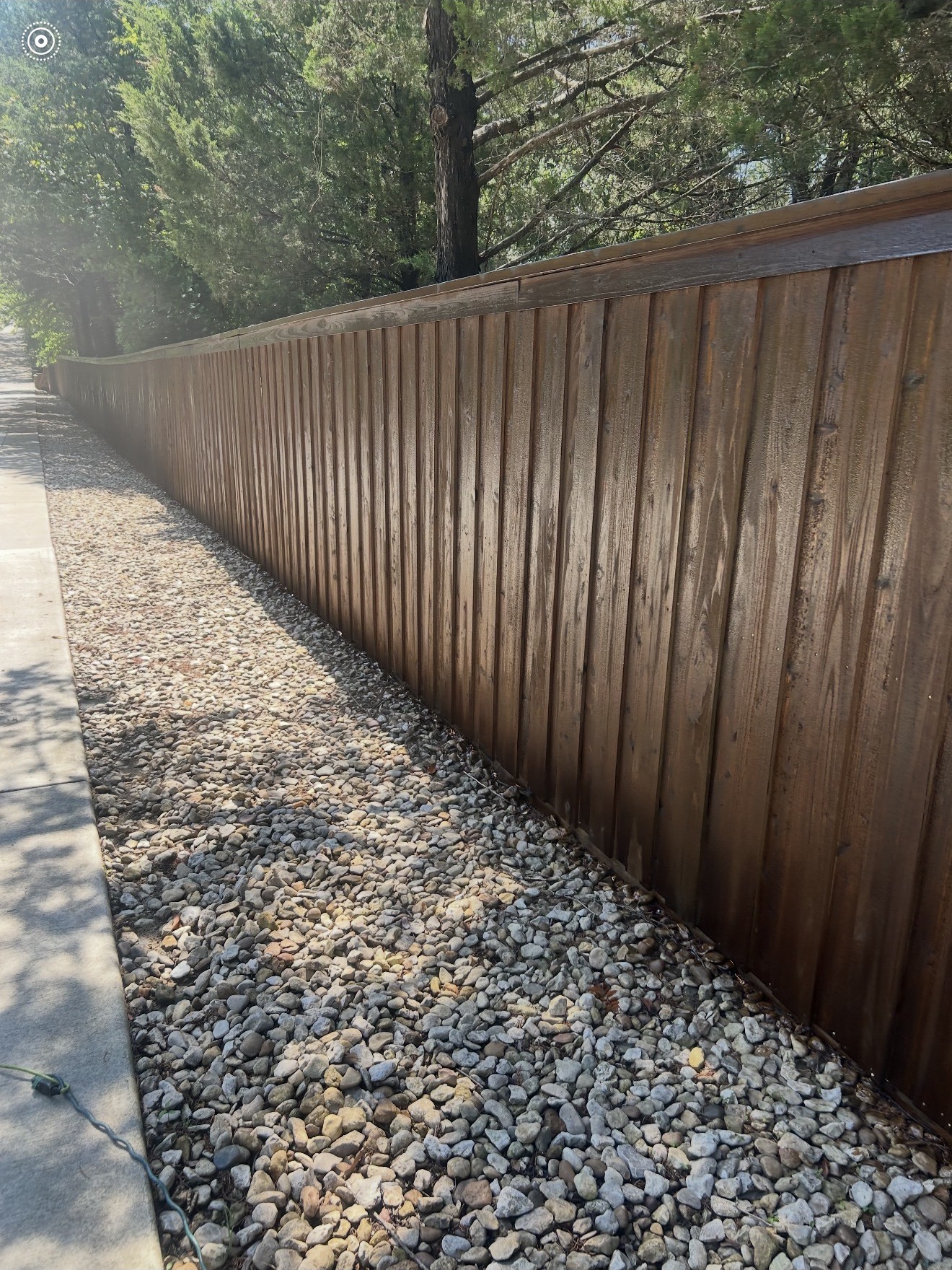 Long finished stained wood fence alongside a decorative stone border