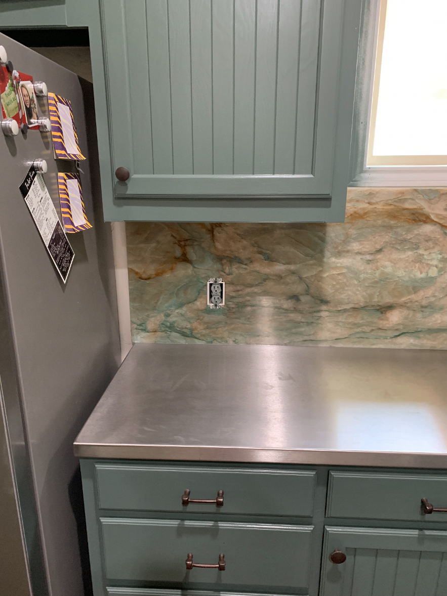 Completed kitchen with stainless steel countertops, a marble backsplash and refrigerator