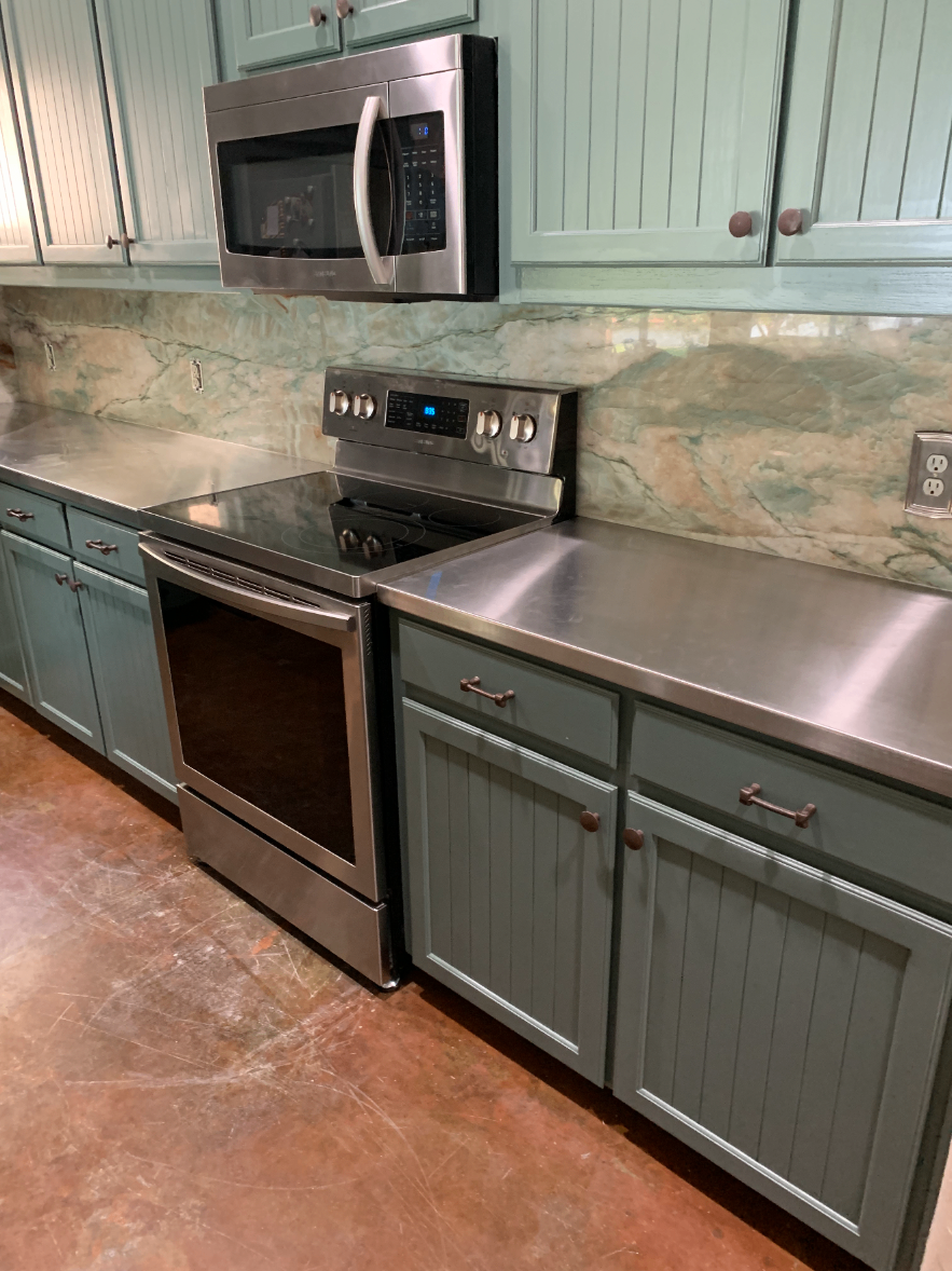 Completed kitchen with stainless steel countertops, a marble backsplash, microwave and range