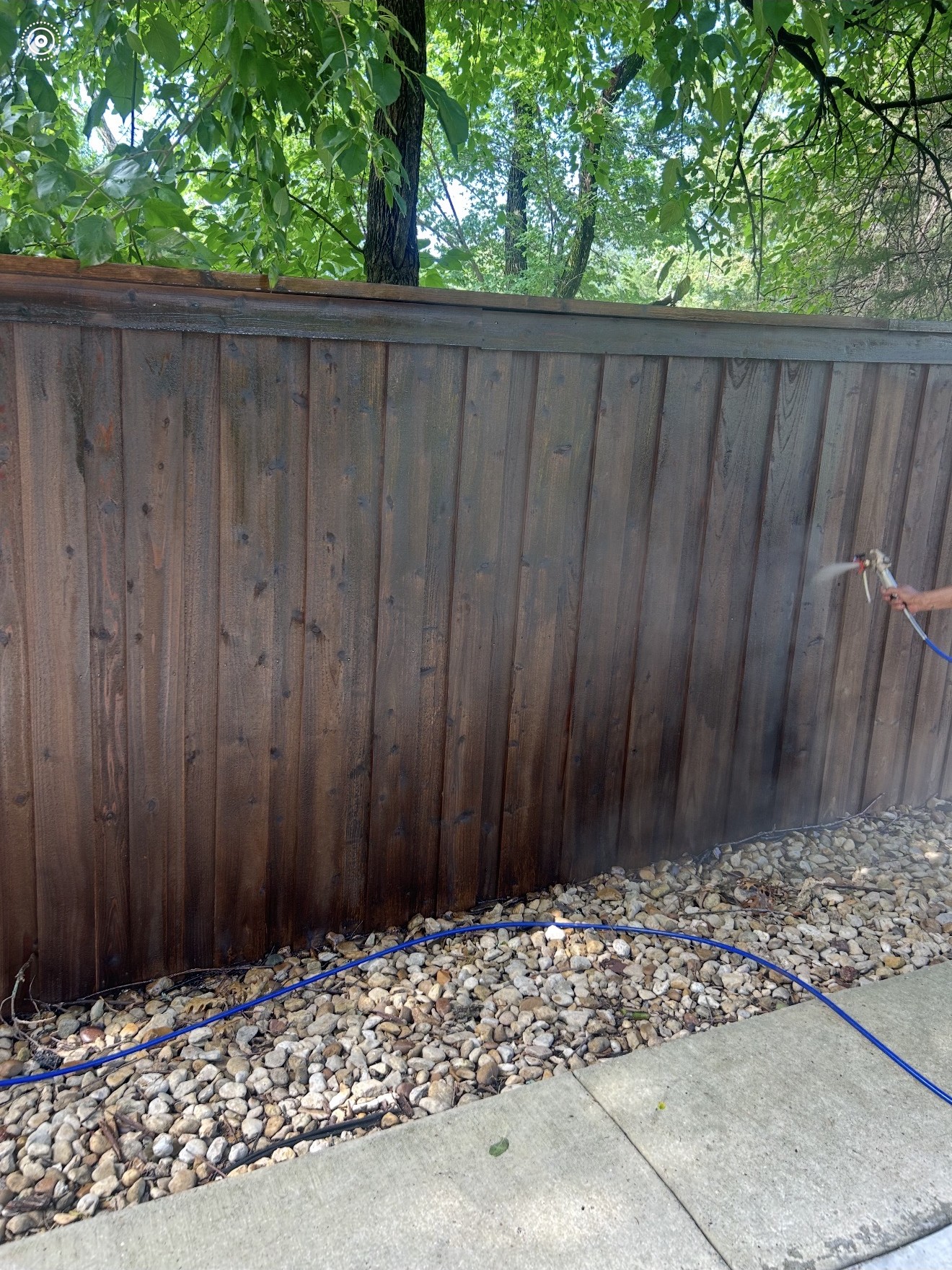 Worker actively spraying stain onto a wood fence