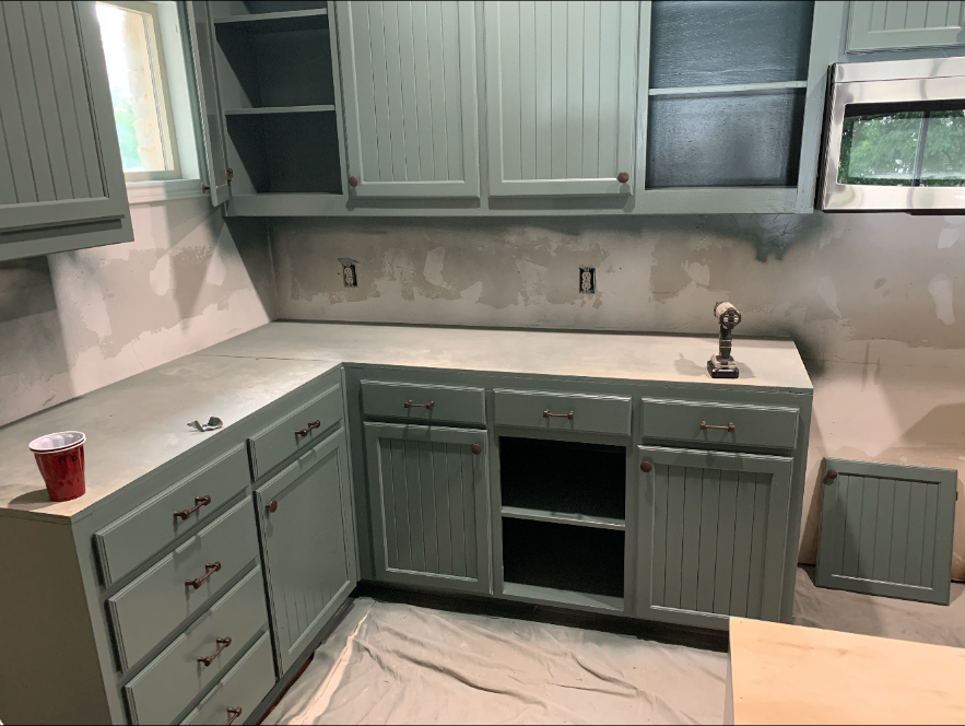 Kitchen mid-renovation with drop cloths on the floor, unfinished walls and cabinets awaiting final hardware