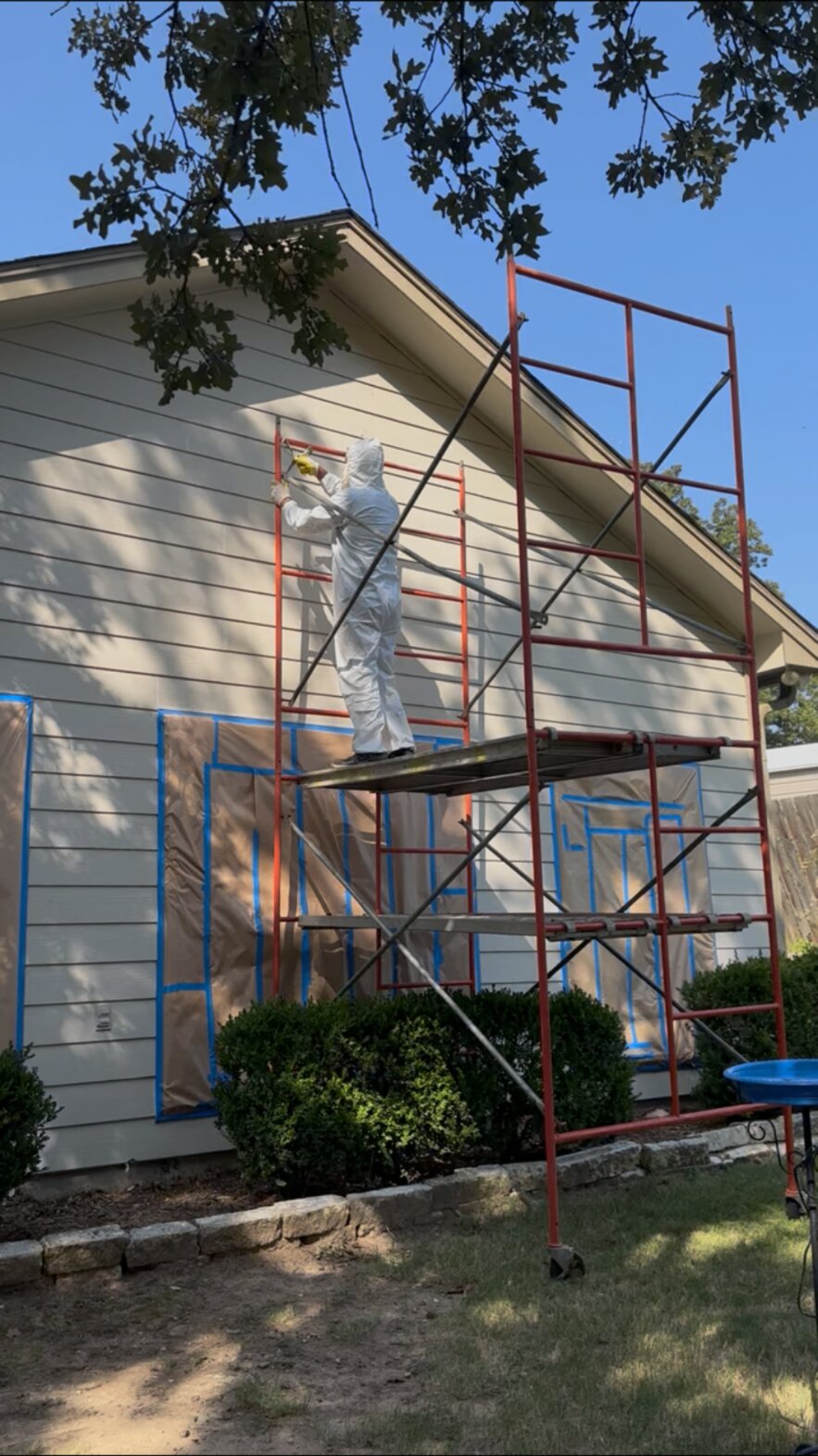 Painter on scaffolding painting the siding of a house with windows masked