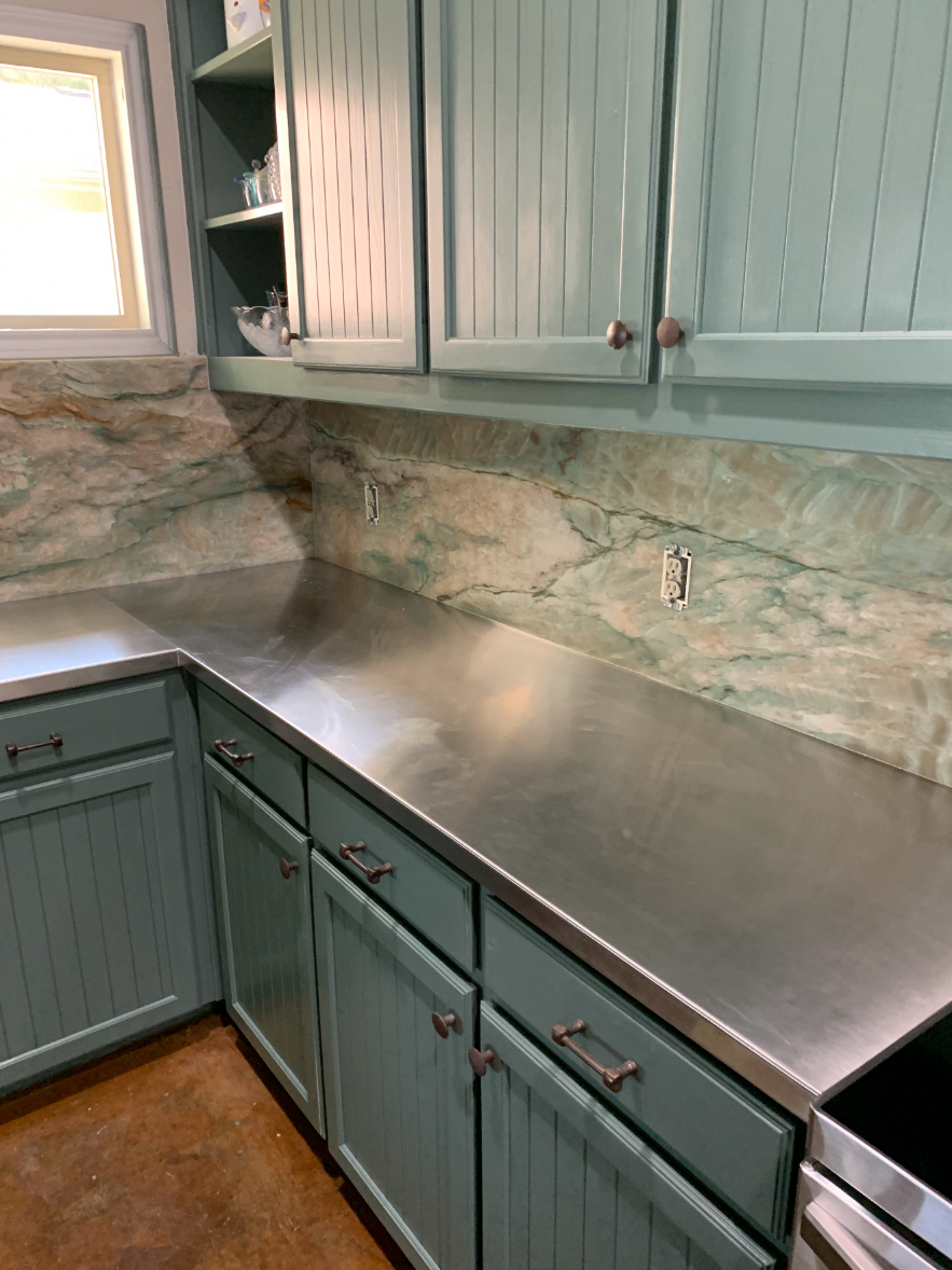 Completed kitchen with light green beadboard cabinets, stainless steel countertops and a marble backsplash